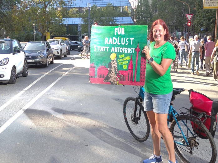 Auf einer Demo sieht man eine Frau auf der Demo von Fridays for Future mit einem Plakat auf den eine Fahhradfahrerin im Hintergrund mit der Skyline von Frankfurt abgebildet ist. 